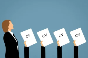 Hands lifting up CV's whilst recruiter walks past symbolizing competition in the amount of job seekers